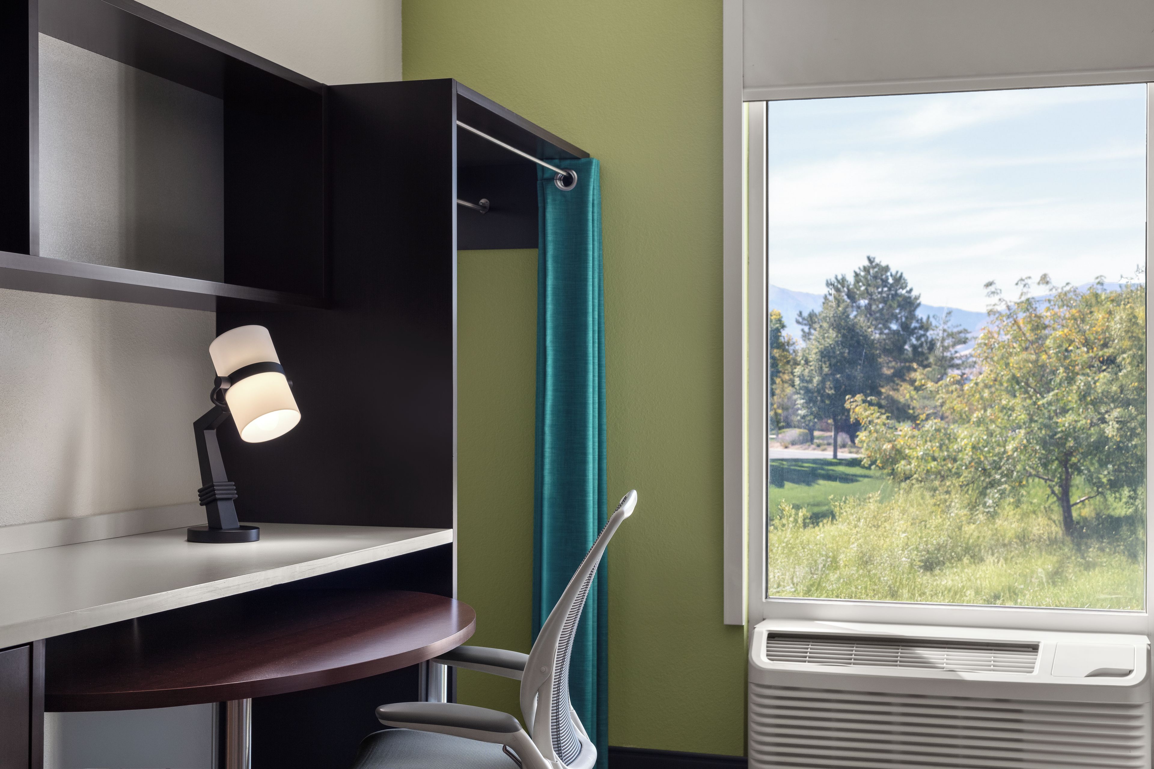 A room with a desk, a chair, a window with a view of trees, and a wall with a green accent.