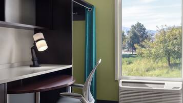 A room with a desk, a chair, a window with a view of trees, and a wall with a green accent.