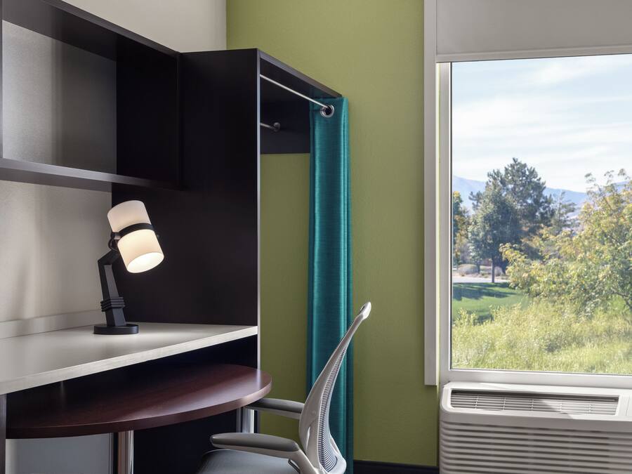 A room with a desk, a chair, a window with a view of trees, and a wall with a green accent.