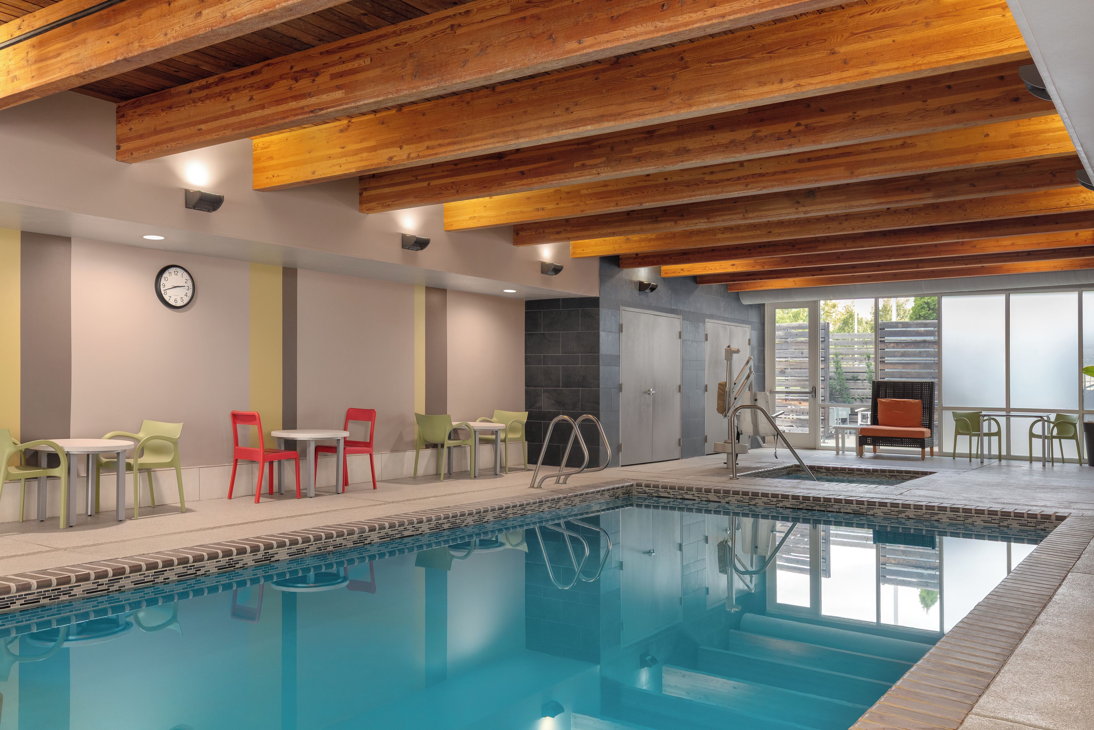 A swimming pool with a tiled edge, a clock on the wall, and a seating area with chairs and tables.