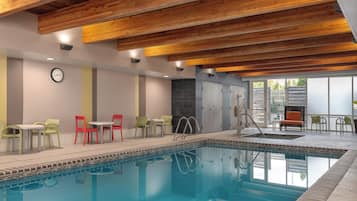 A swimming pool with a tiled edge, a clock on the wall, and a seating area with chairs and tables.