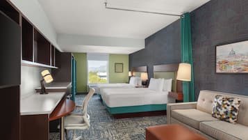 A hotel room with two beds, a desk, a chair, a sofa, and a large window offering a view.