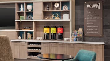 Eine moderne Küche mit eingebauten Kaffeemaschinen, ein Essbereich mit rundem Tisch und einem Schild mit der Aufschrift 'HOME2 GUARANTEE'.