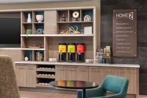 A modern kitchen with built-in coffee machines, a dining area with a round table, and a 'HOME2 GUARANTEE' sign.