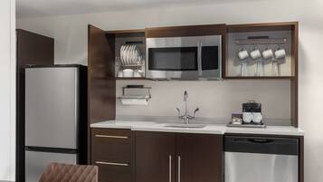 A compact kitchen with a refrigerator, microwave, coffee maker, and dish drying rack.