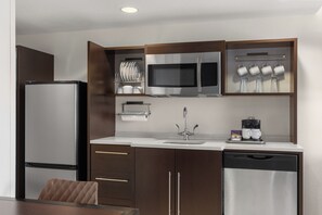 A compact kitchen with a refrigerator, microwave, coffee maker, and dish drying rack.