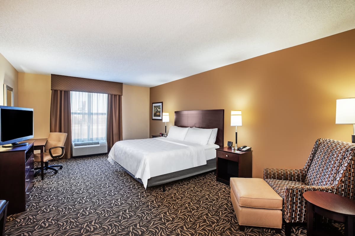 A hotel room with a large bed, a desk with a TV, a chair, a sofa, and a window with curtains.