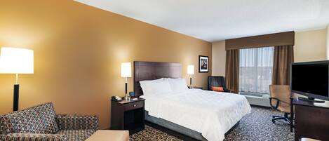 A hotel room with a bed, a sofa, a desk, a television, and a window with curtains.