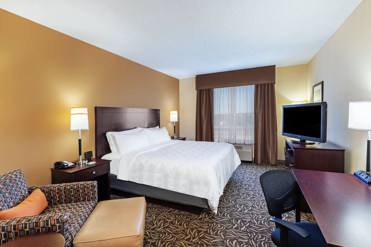 A hotel room with a large bed, a desk, a television, a chair, and a sofa.