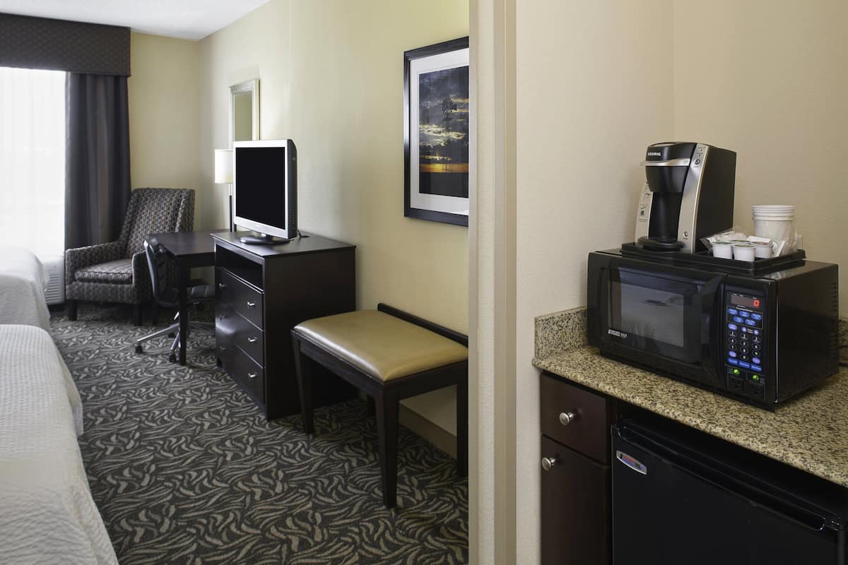 A hotel room with a bed, a desk with a computer, a chair, a television, a coffee maker, and a microwave.