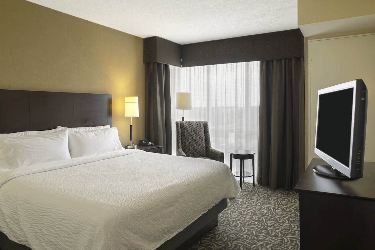 A hotel room with a large bed, a television on a desk, a chair, and a small table.