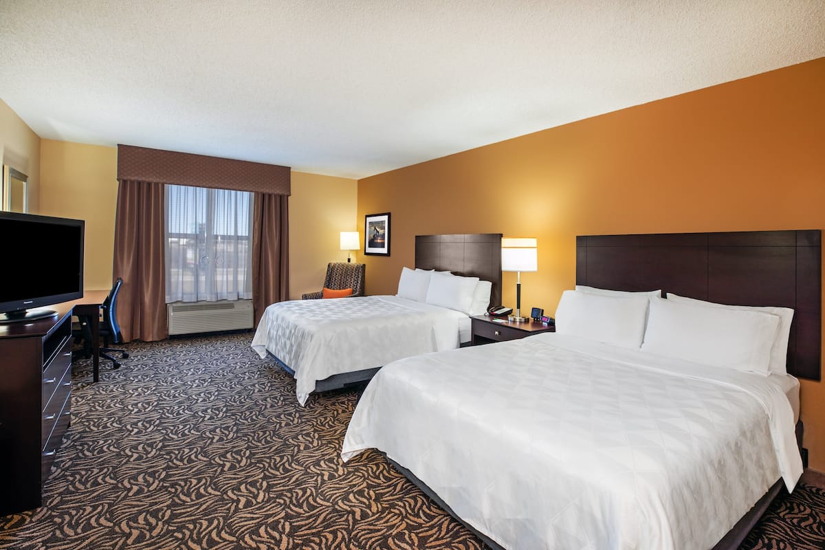 A hotel room with two beds, a TV, a desk, and a window with curtains.