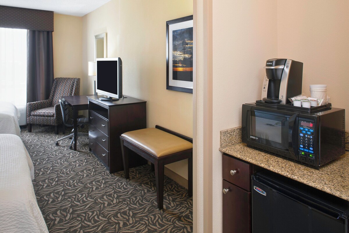 A hotel room with a bed, a desk with a computer, a chair, a television, a coffee maker, and a microwave.