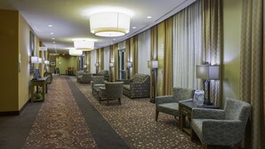 A hotel lobby with a carpeted floor, multiple armchairs, tables, and lamps.