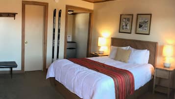 A hotel room with a large bed, two bedside lamps, a bench, and a door.