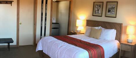 Una habitación de hotel con una cama grande, dos lámparas de noche, un banco y una puerta.
