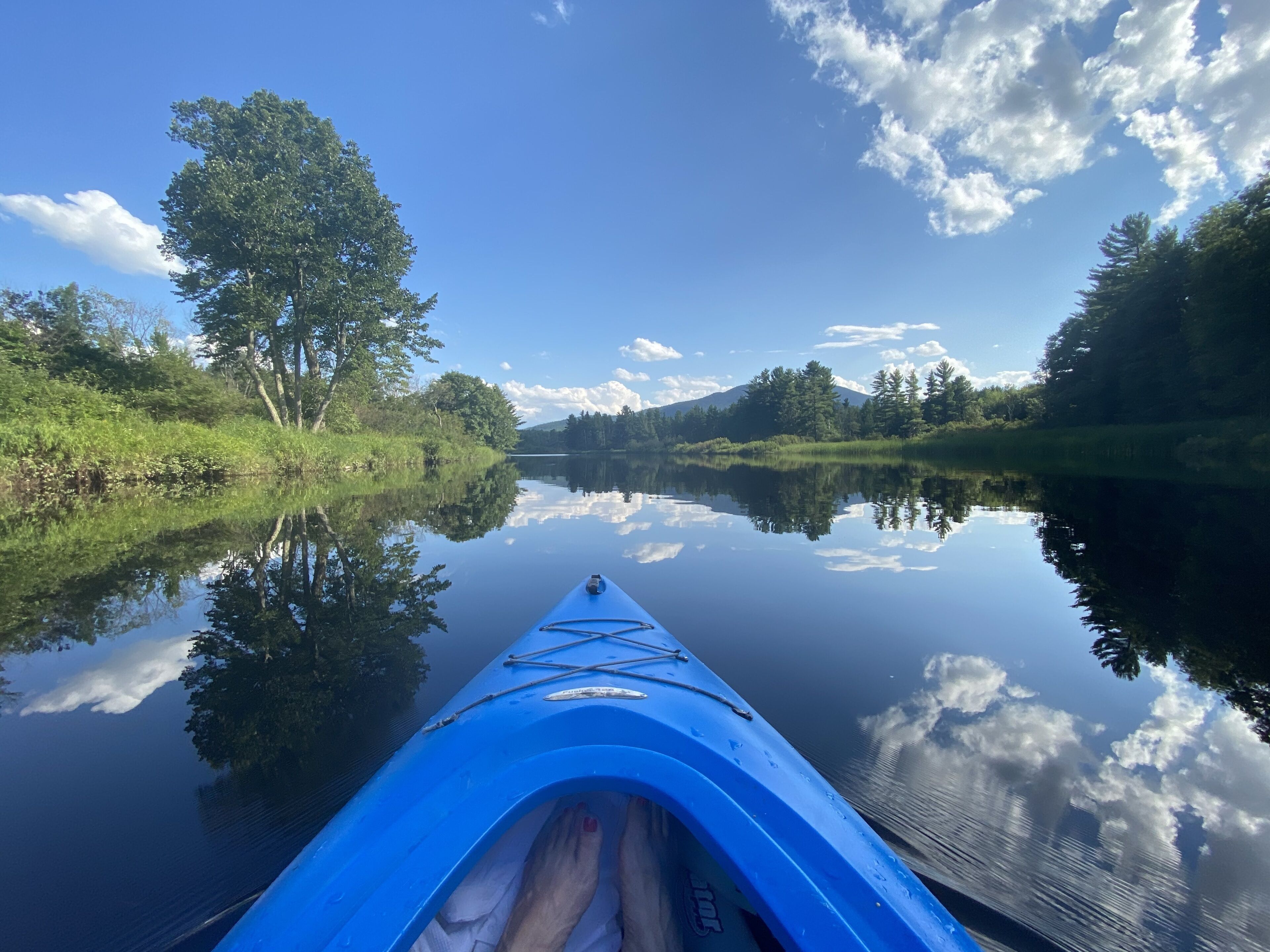 Una canoa en un río tranquilo con reflejos de árboles y cielo.