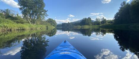 Una canoa en un río tranquilo con reflejos de árboles y cielo.