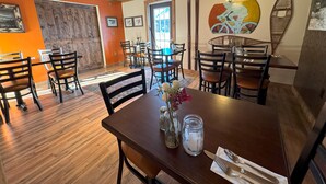 A restaurant interior with wooden floors, orange walls, and a wooden ceiling. Tables and chairs are arranged for dining. - Cadence Lodge at Whiteface (Wilmington)