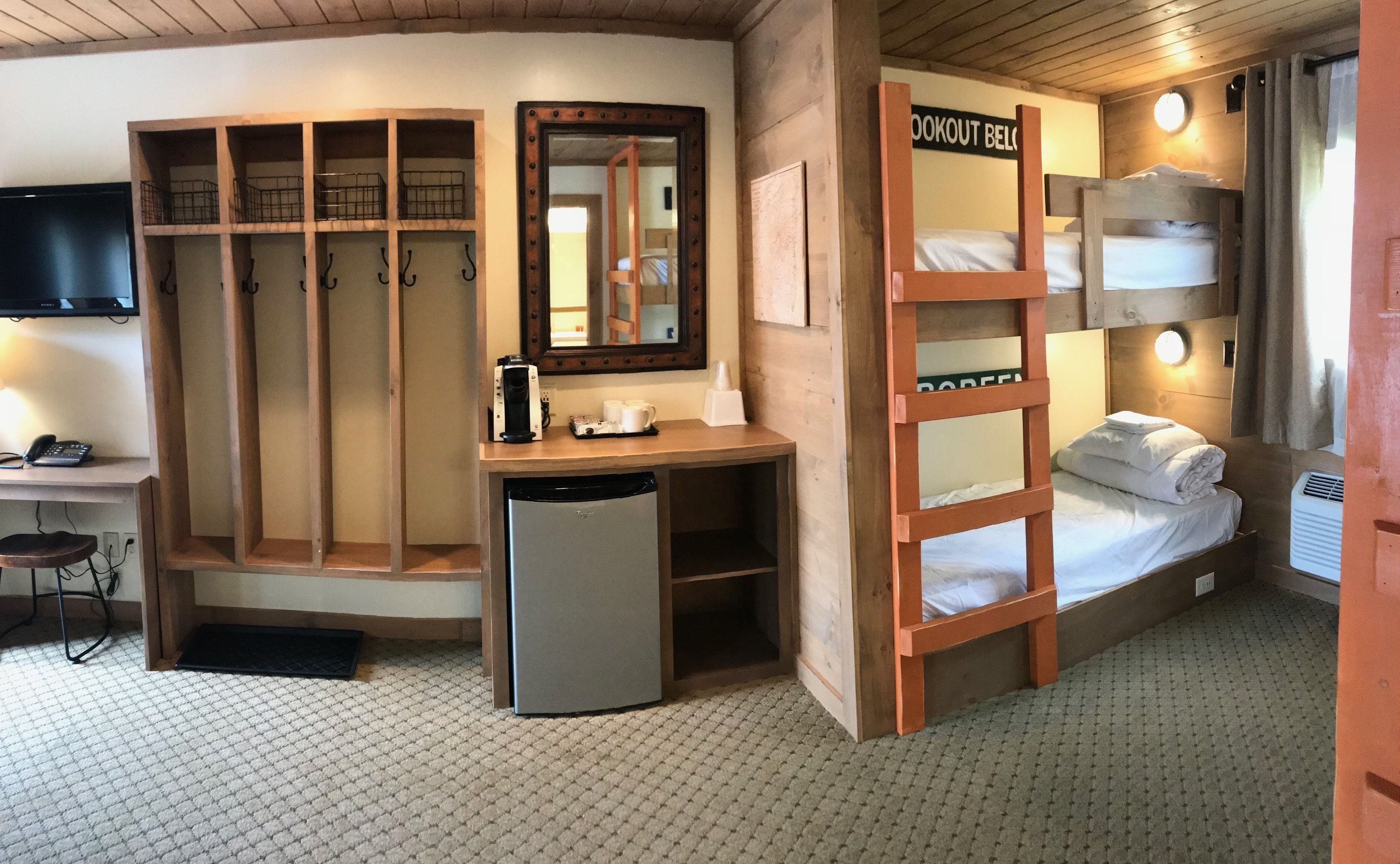 A compact room with bunk beds, a desk with a computer, a mirror, and a television.