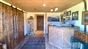 A wooden interior with a ski-themed decor, including skis and a ski rack, a patterned rug, and a reception desk with a vase of flowers. - Cadence Lodge at Whiteface (Wilmington)