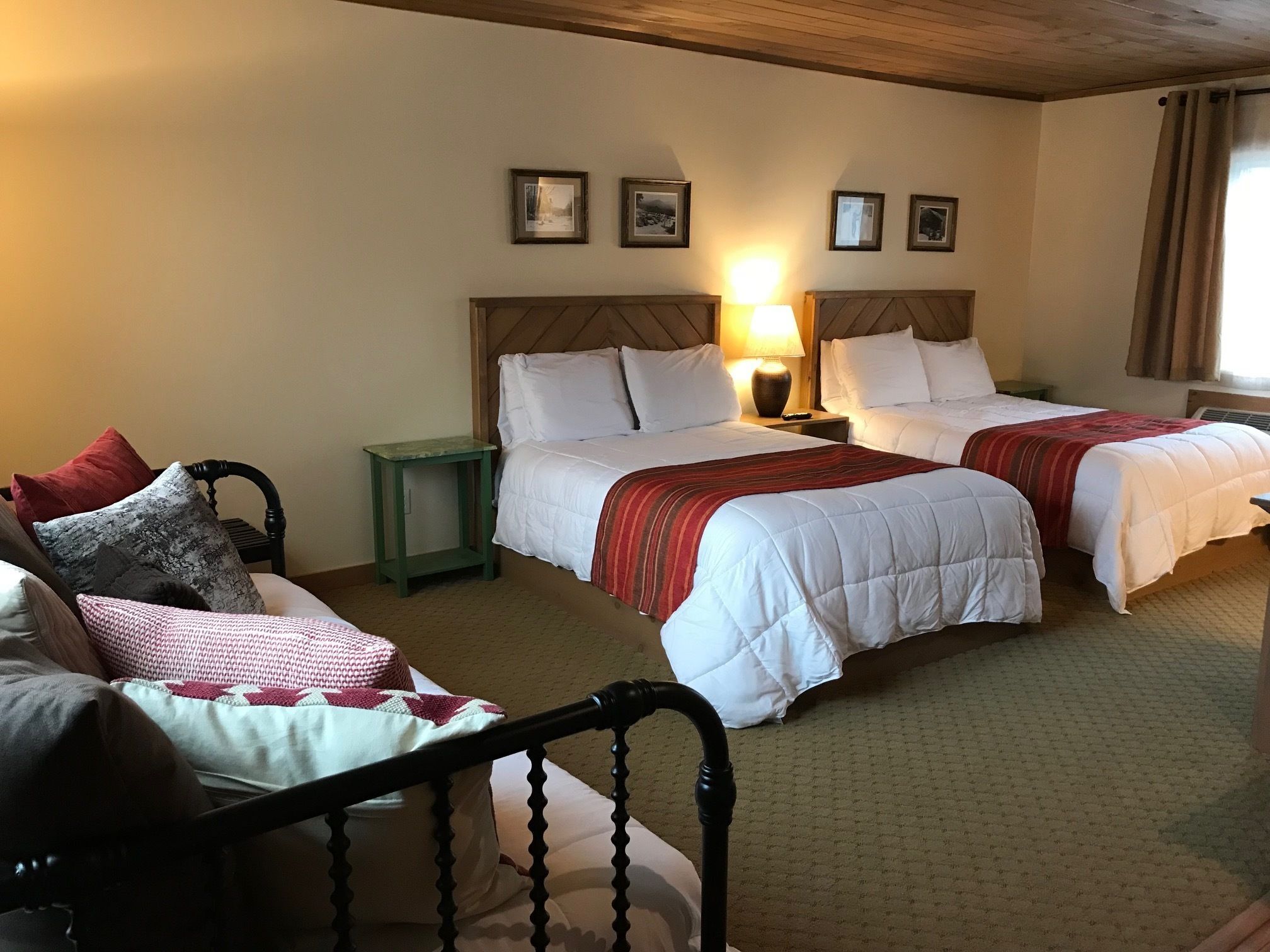 A hotel room with two beds, a small green nightstand, a wooden chair, and a wooden headboard.