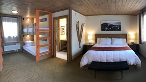 A hotel room with bunk beds, a large bed with a red blanket, a headboard, bedside lamps, a wall-mounted picture, and a wooden ceiling. - Cadence Lodge at Whiteface (Wilmington)