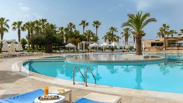 Zona junto a la piscina con sillones de descanso, sombrillas y una mesa de comedor con comida y bebidas.