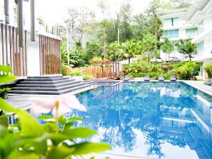Una piscina con escalones de acceso, rodeada de abundante vegetación y un edificio moderno.