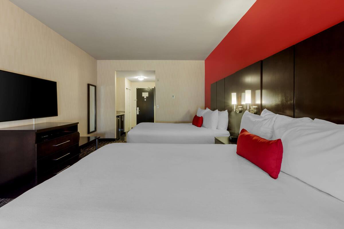 Habitación de hotel con dos camas, un televisor de pantalla plana, un aparador y una pared de acento roja.