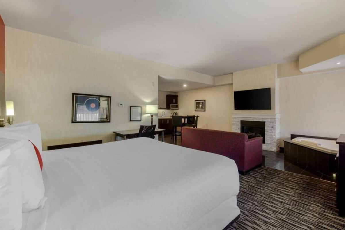 Una habitación de hotel con una cama grande, un escritorio, una silla, un sofá, una chimenea y un televisor montado en la pared.