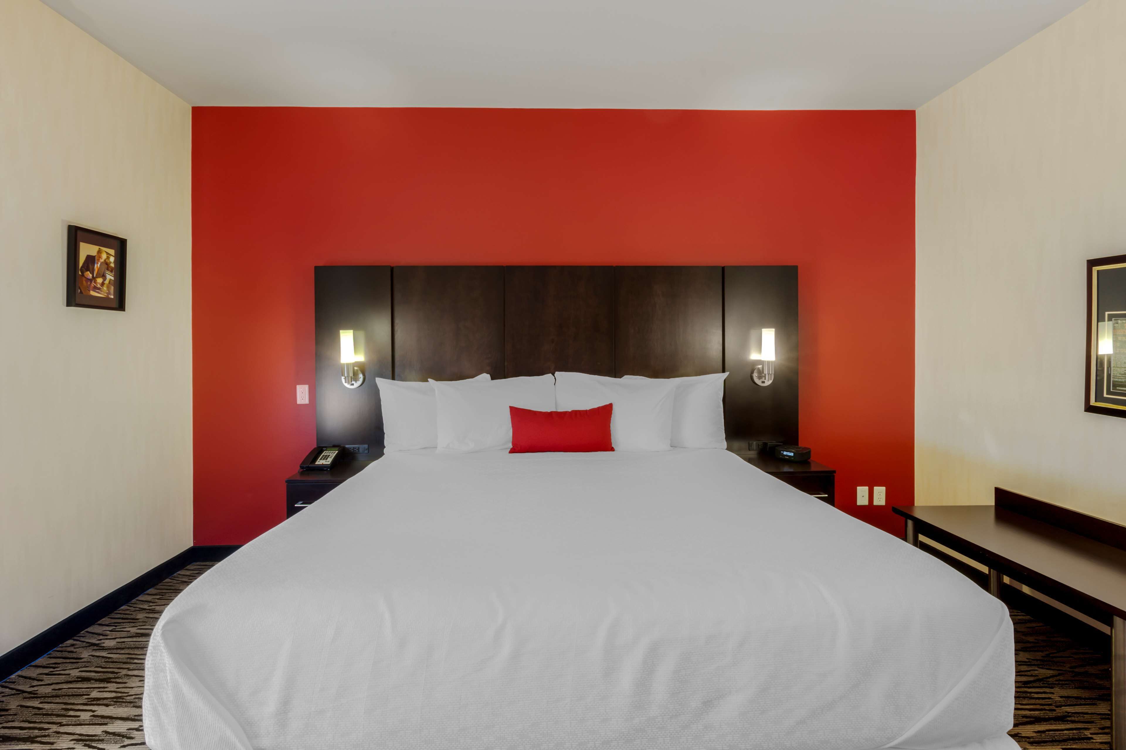 A hotel room with a large bed, red accent walls, and two bedside tables with lamps.