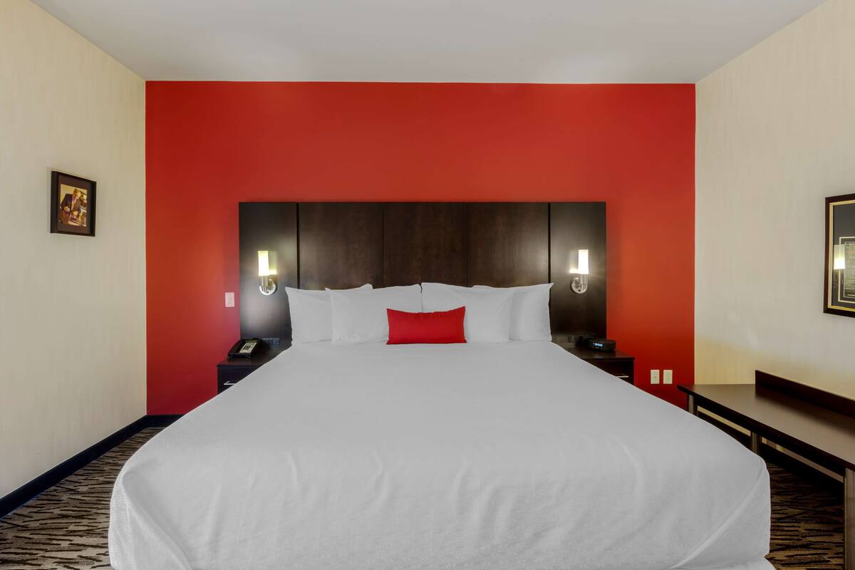 A hotel room with a large bed, red accent walls, and two bedside tables with lamps.