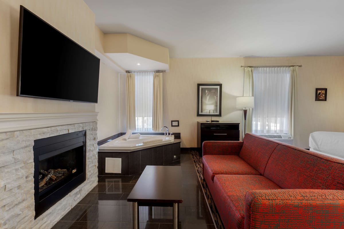 Habitación de hotel con televisor de pantalla plana, chimenea, sofá, cama y baño con bañera, además de una ventana con cortinas.