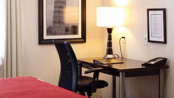 Habitación de hotel con cama, escritorio con silla, lámpara, un cuadro con la Torre de Pisa y un documento enmarcado en la pared.