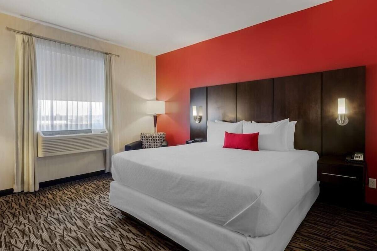 Habitación de hotel con una cama grande, una mesita de noche, una lámpara y una ventana con cortinas.
