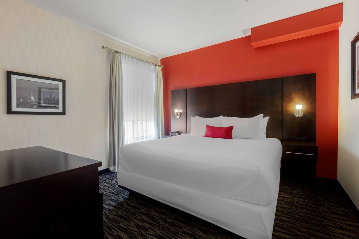 A hotel room with a large bed, a desk, a nightstand, and a wall-mounted lamp.