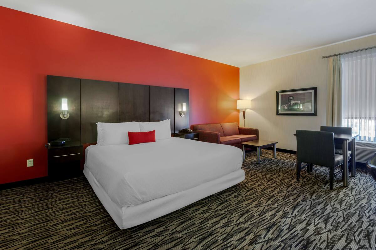 Habitación de hotel con una cama grande, una pared de acento roja, un escritorio, una silla y un sofá.