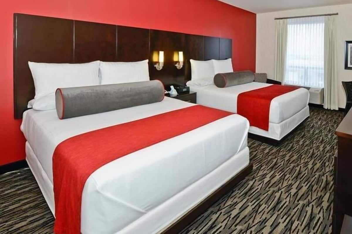 Habitación de hotel con dos camas, una pared roja, alfombra estampada y una ventana con cortinas.
