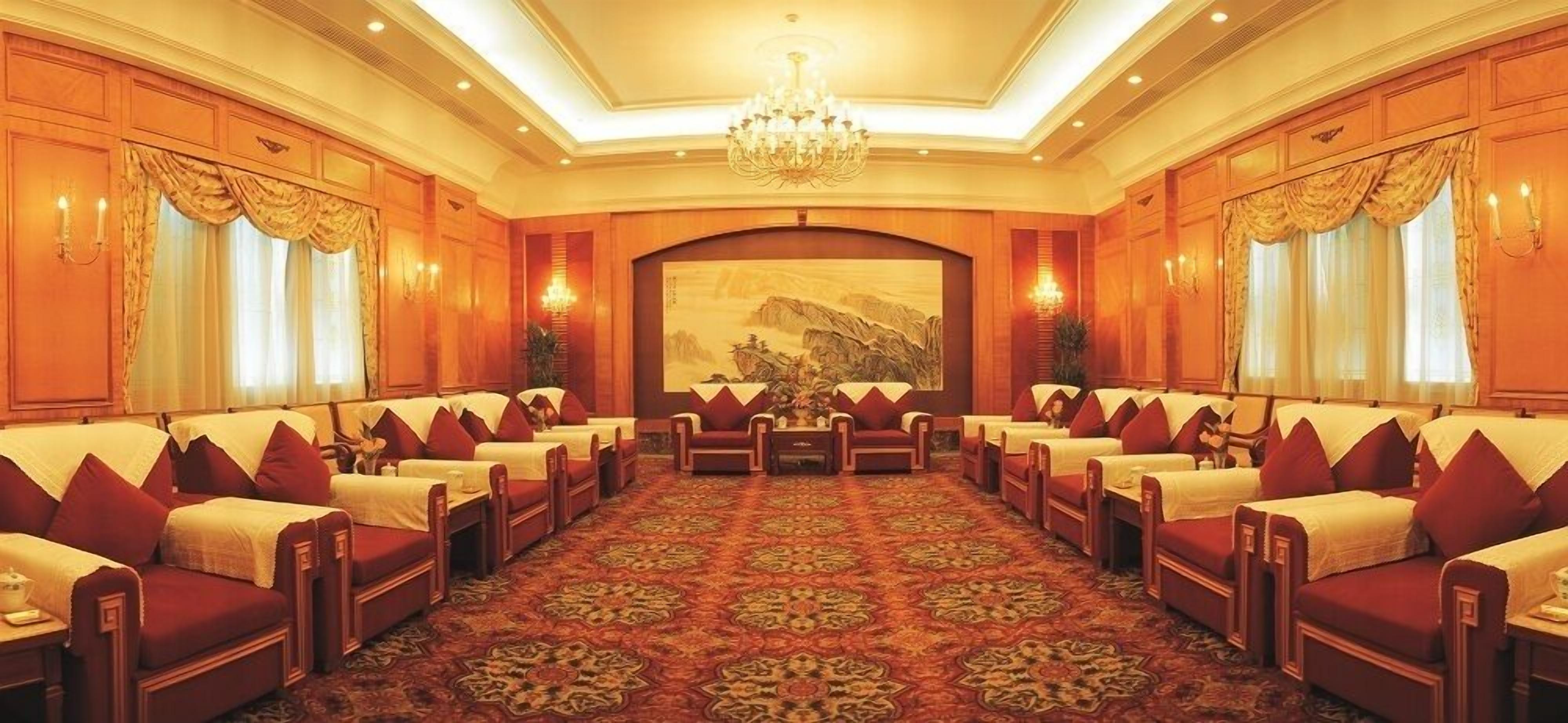 A conference room with rows of red sofas, a patterned carpet, and a large painting on the wall.