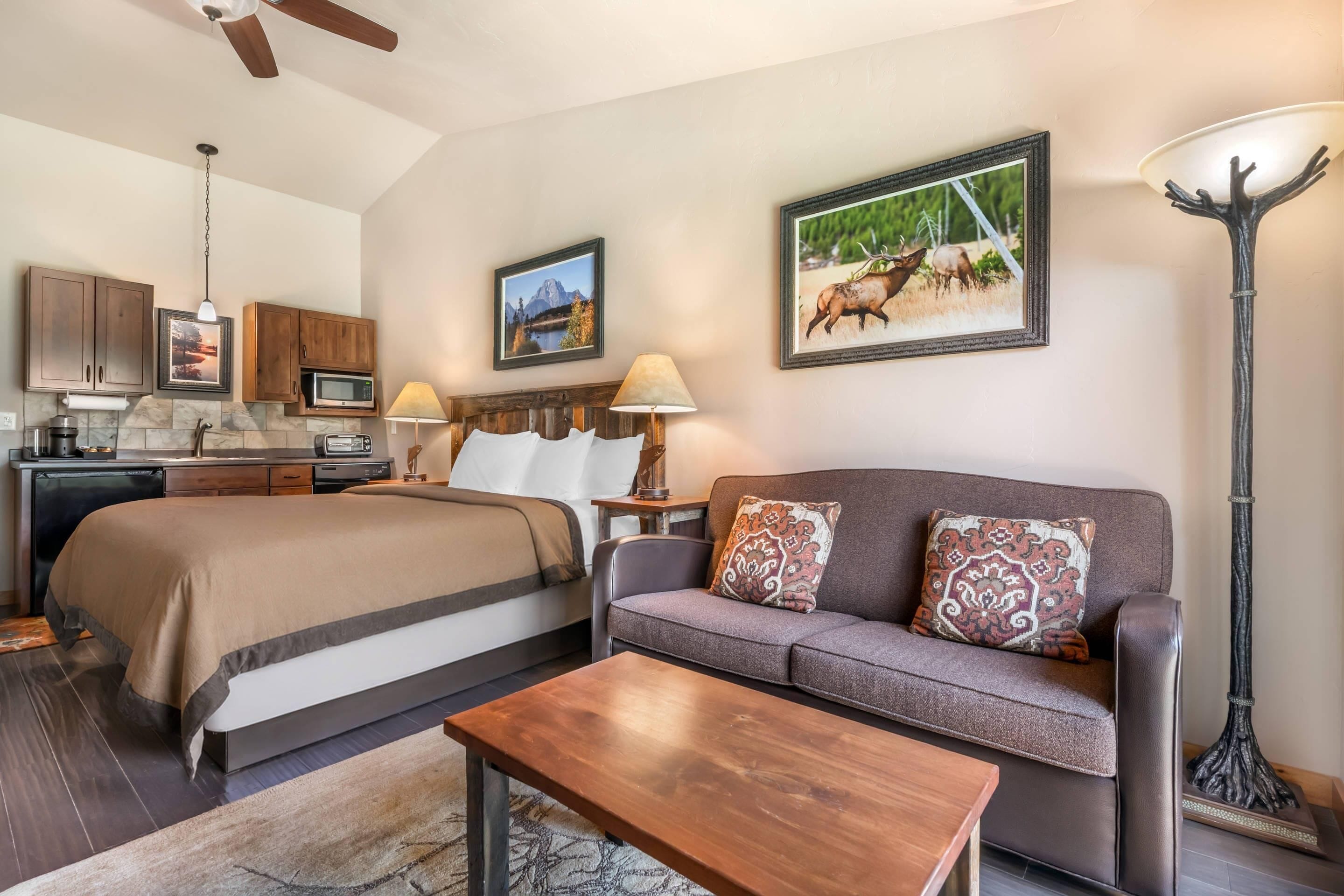 A well-lit, modern bedroom with a large bed, a sofa, and a coffee table. There is a kitchen area with cabinets and a microwave.