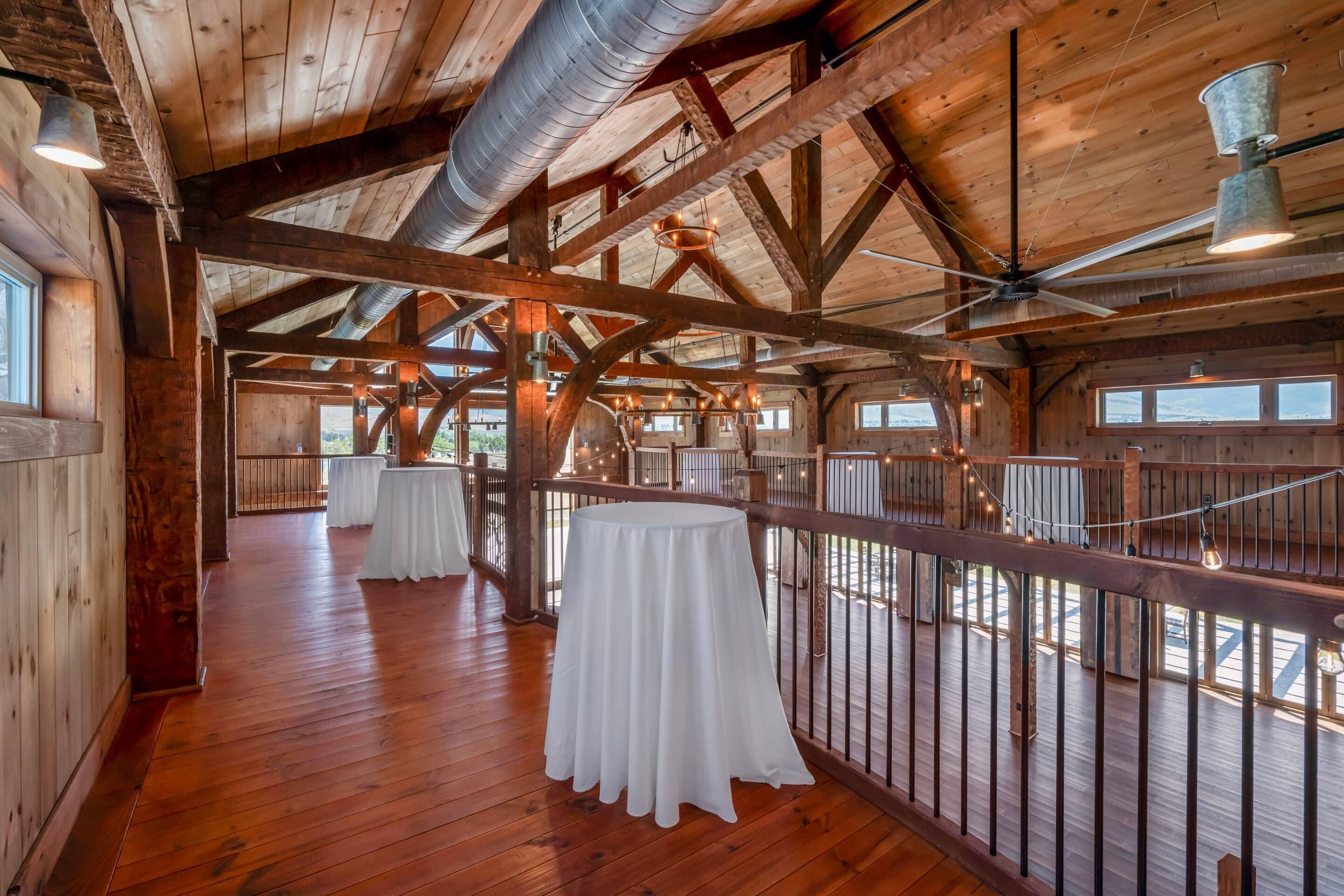 A spacious wooden interior with high ceilings, exposed beams, and a balcony overlooking a scenic view.