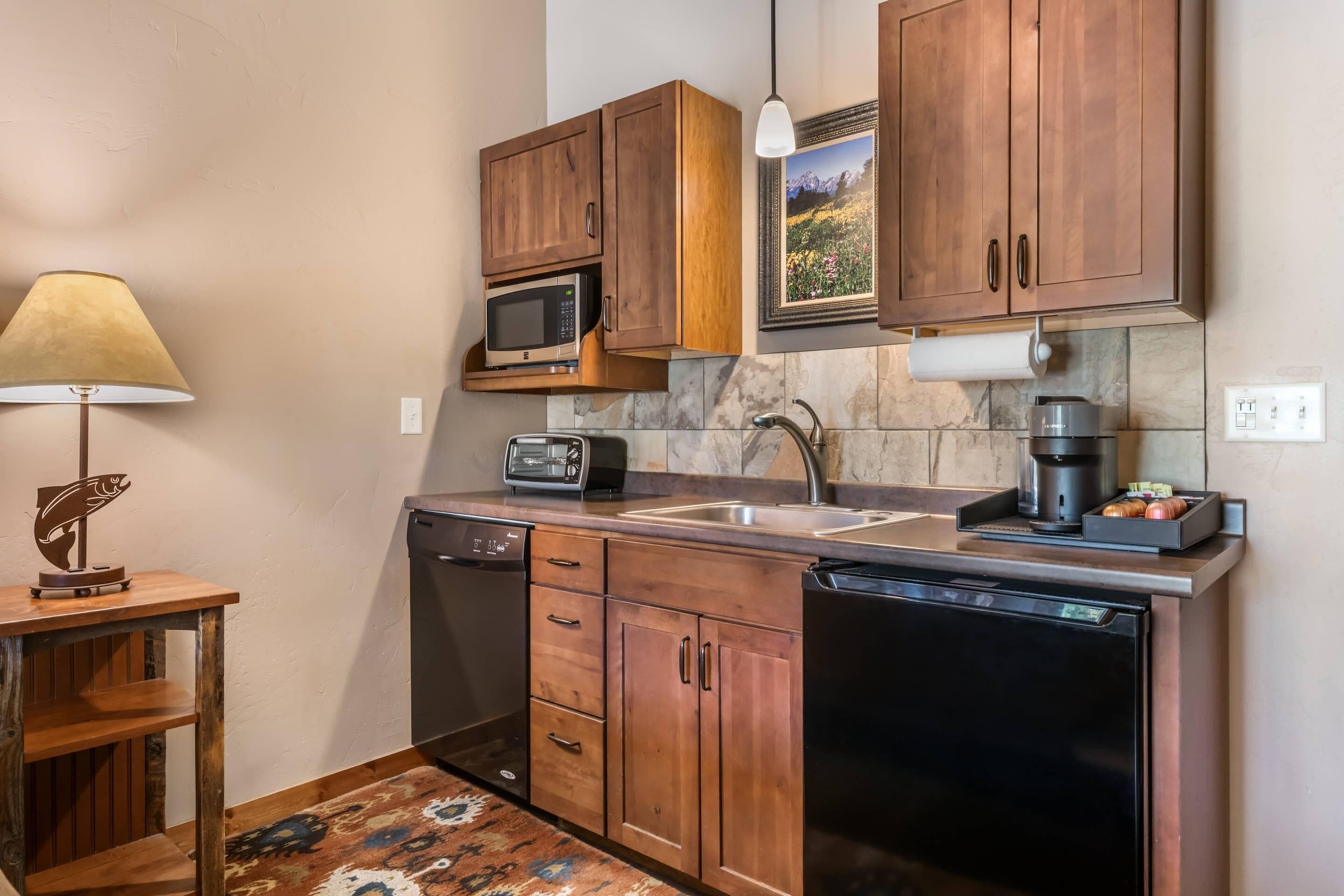 A compact kitchen with wooden cabinets, a microwave, a toaster, a coffee maker, and a dishwasher.