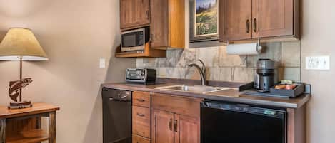 A compact kitchen with wooden cabinets, a microwave, a toaster, a coffee maker, and a dishwasher.