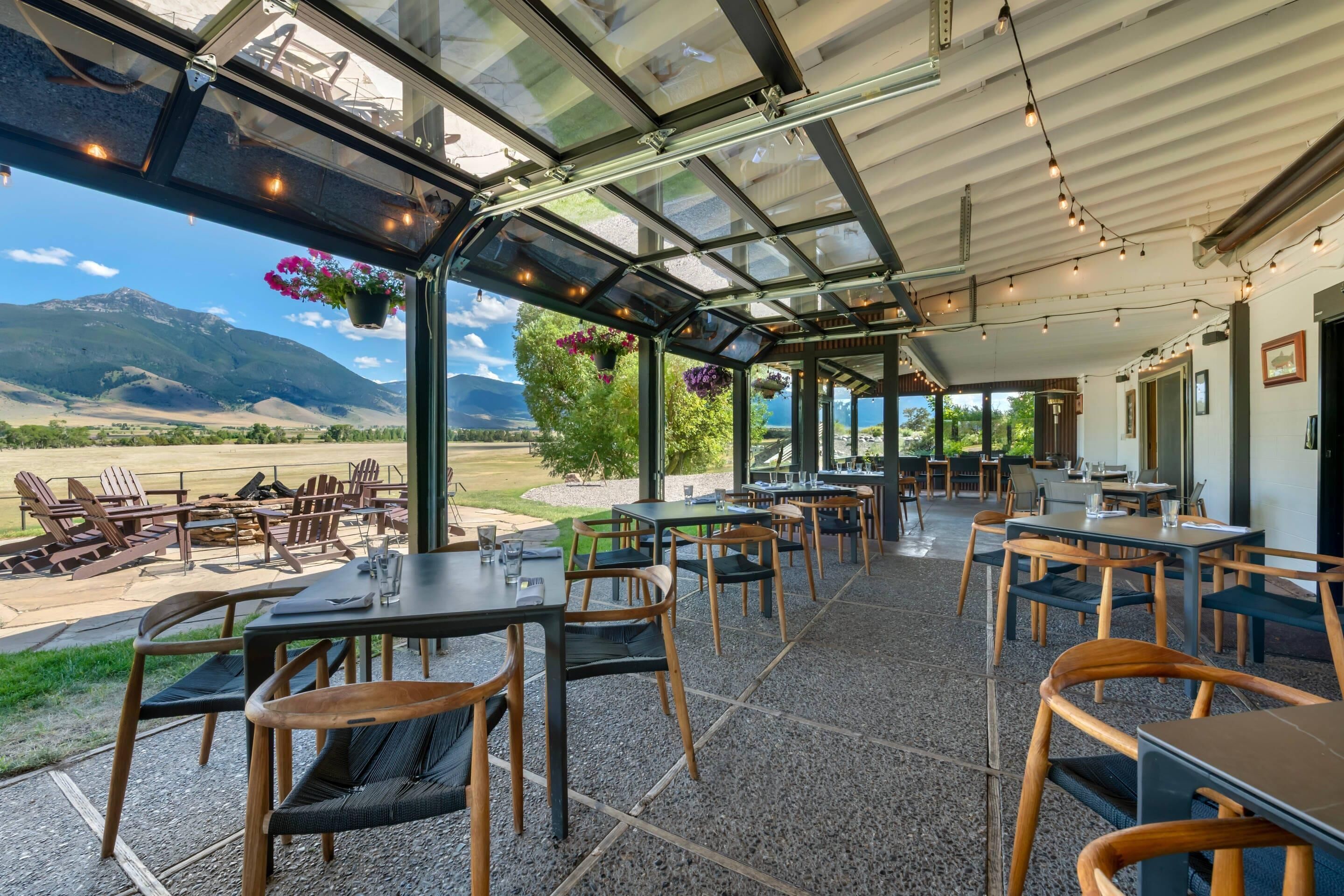 An outdoor dining area with tables and chairs, a glass ceiling, and a view of mountains.