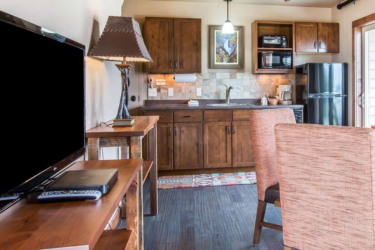 A compact kitchen with wooden cabinets, a microwave, a refrigerator, and a ceiling fan.