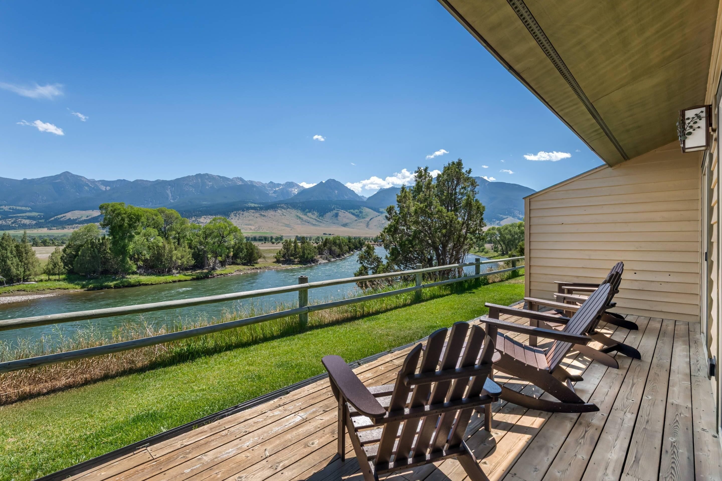 Une terrasse en bois avec des fauteuils Adirondack, donnant sur une rivière et des montagnes.