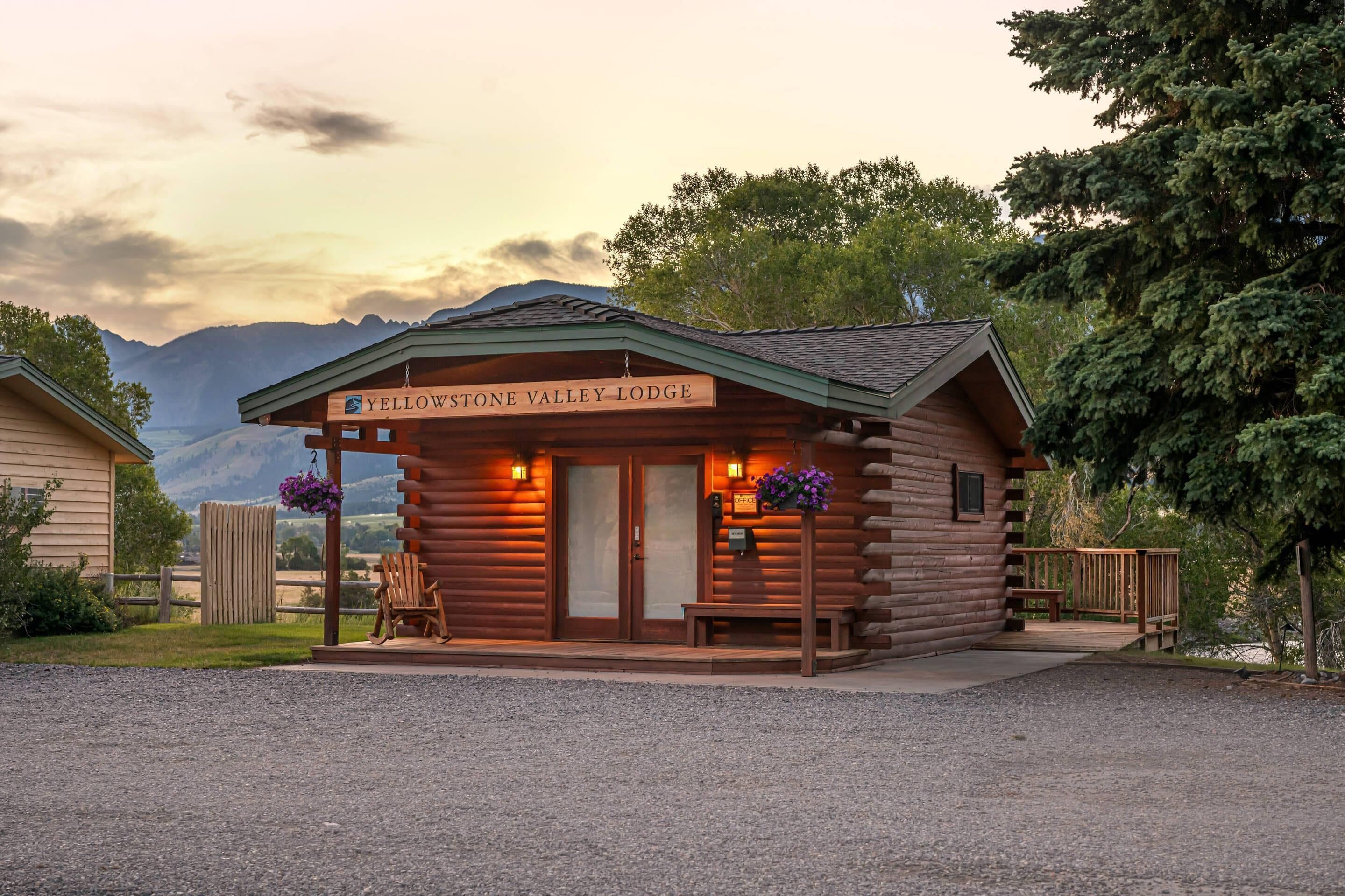 Una cabaña de troncos con un letrero que dice 'Yellowstone Valley Lodge' y una vista de montañas al fondo.