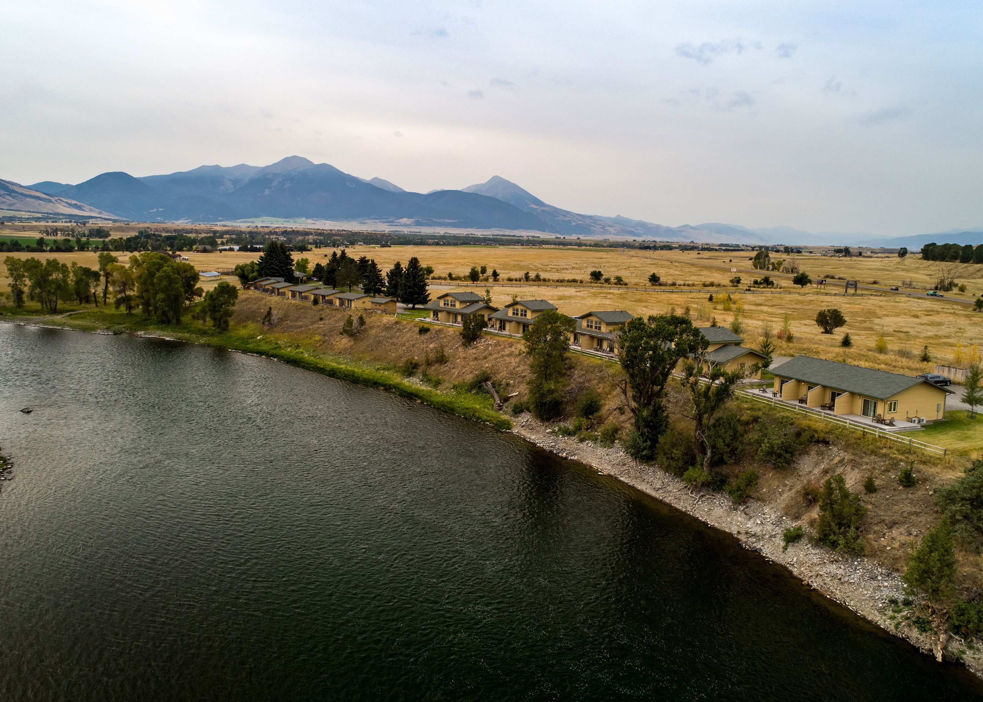 A riverside property with multiple houses, a grassy field, and mountains in the background.
