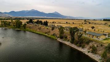 A riverside property with multiple houses, a grassy field, and mountains in the background.